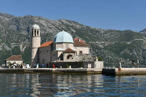       Stone church of Our Lady of the Rocks sits on an islet amid calm bay waters backed by rugged mountains.
  