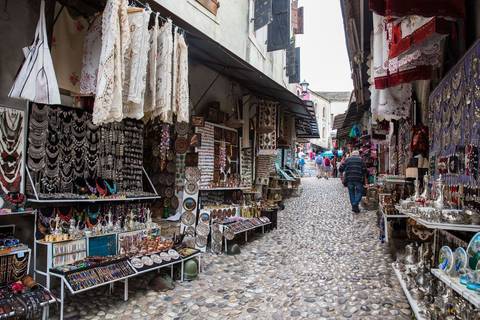       Bustling craft bazaar with hanging lace, jewelry and souvenirs along a cobbled lane.
  