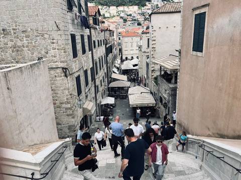       Stone staircase alley in Dubrovnik filled with tourists ascending between historic buildings.
  