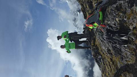       Two trekkers in bright shirts celebrate atop a rocky Andean ridge with snowy peaks behind.
  