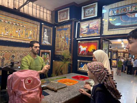       Papyrus art shop where a guide demonstrates painting techniques to an attentive family.
  