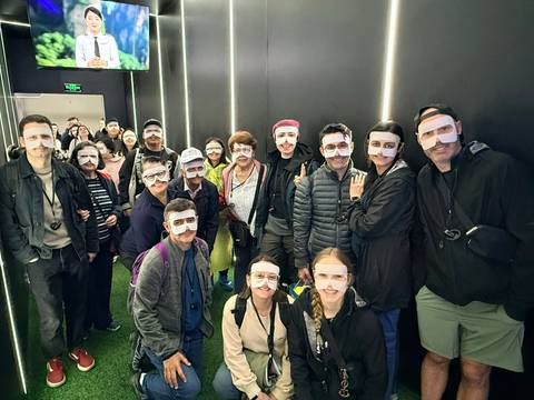       Group wearing humorous paper masks posing indoors under dim lighting.
  