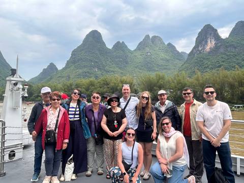       Group portrait on riverboat with dramatic karst peaks rising behind them.
  