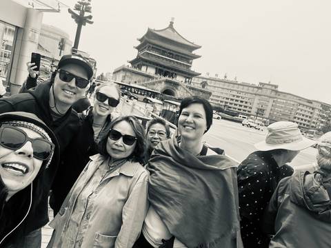       Black-and-white selfie of travelers in front of a historic Chinese tower at a busy city intersection.
  