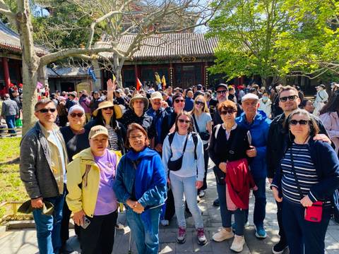       Large tour group gathers in a courtyard of a traditional Chinese complex amid many other visitors.
  