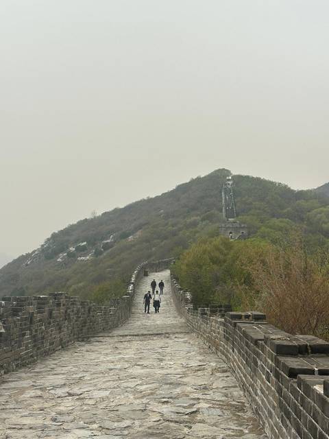       Travelers walking along a misty section of the Great Wall that snakes over a tree-covered ridge.
  