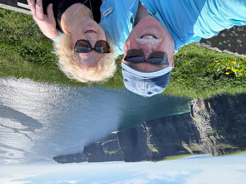       Couple selfie with the towering Cliffs of Moher and shimmering Atlantic waters in the background.
  
