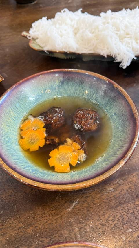       Steaming bowl of clear broth with meatballs and carrot flower garnishes.
  