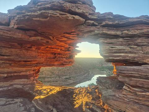       Natural sandstone window framing a river gorge glowing orange in early light
  
