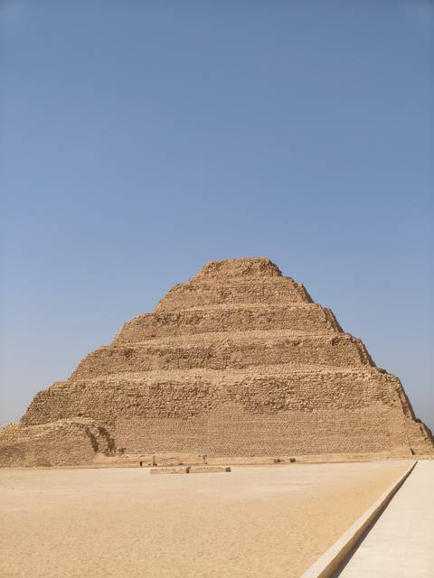       The Step Pyramid of Djoser rises in layered limestone tiers against a cloudless sky.
  