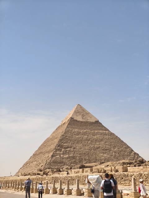       Pointed apex of a Giza pyramid stands against pale sky, highlighting weathered stones.
  