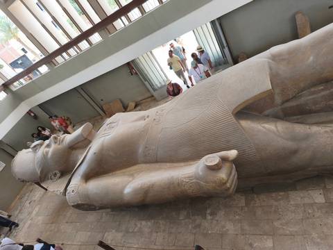       Massive reclining statue of Ramses II in indoor museum with visitors looking on.
  