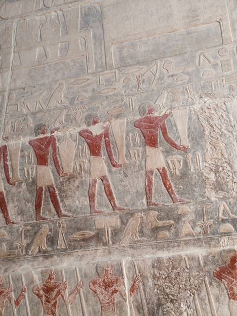       Ancient painted reliefs of Egyptian figures carrying offerings adorn a temple wall.
  