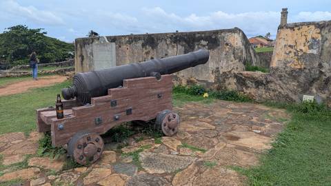       Old black cannon on a wooden carriage overlooks the ramparts of Galle Fort, with a beer bottle placed on it.
  