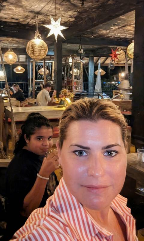       Close-up selfie in a cosy restaurant showing an adult woman in front with a child and diners in the background.
  