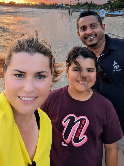       Outdoor selfie of three travellers smiling with evening sky and sandy ground behind them.
  
