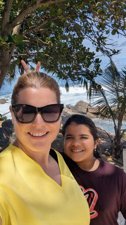       Smiling mother and daughter selfie with crashing Indian Ocean waves and palm fronds behind them.
  