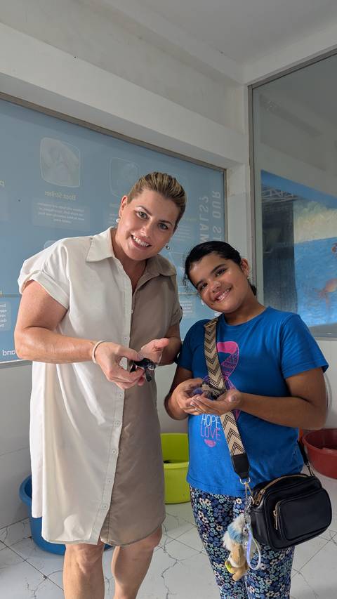       Adult and child proudly holding tiny sea turtles inside a conservation centre.
  