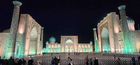      Night view of the illuminated Registan square with three grand madrasas lit in turquoise and gold.
  