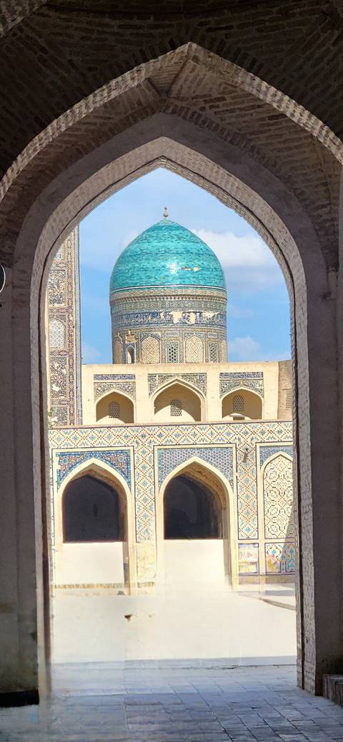       Ornate blue-tiled dome and mosaics framed through a stone arch against a bright sky.
  