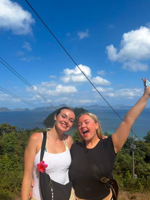       Two friends smile with raised arm against a backdrop of blue sea, islands and cable lines.
  