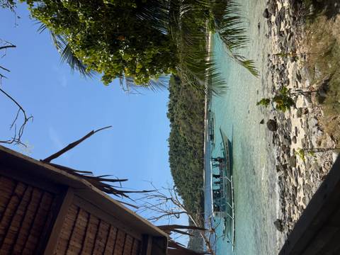       View from a wooden hut across turquoise water to a banca boat and forested shoreline.
  