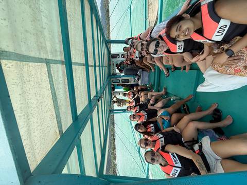       Large tour group seated inside an open-air boat with turquoise water visible through the sides.
  