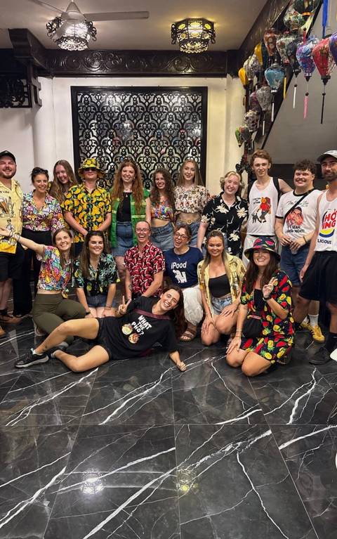       Large group wearing bright tropical shirts smiles for a fun indoor photo.
  