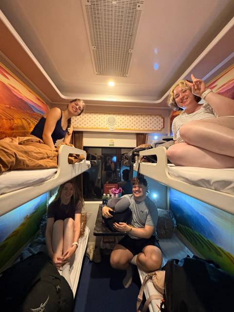       Four travellers relax in cosy bunk beds inside an overnight train cabin.
  