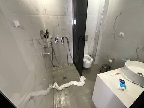       Modern bathroom with water leaking onto the floor and towels blocking the drain.
  