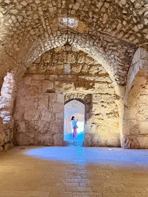       Woman in pink skirt admires light filtering through an ancient stone-arched chamber.
  