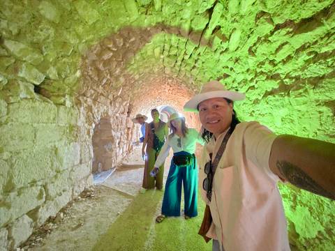       Selfie of four travellers inside a stone tunnel bathed in green and orange lighting.
  