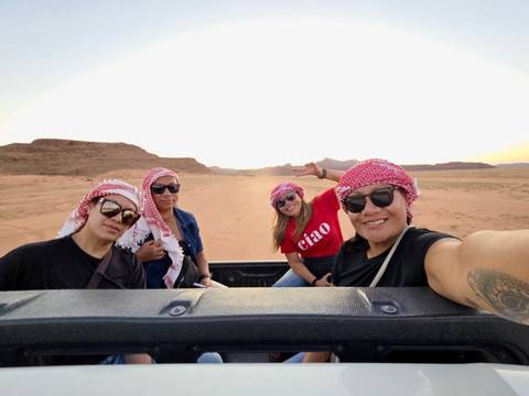       Group of friends in pickup truck take a selfie while speeding across Wadi Rum at sunset.
  