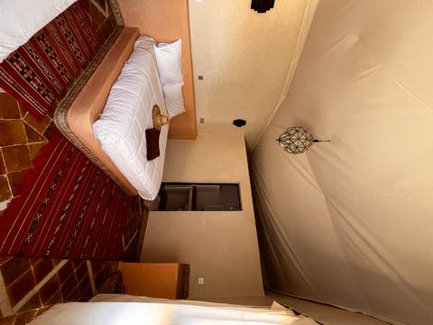       Rustic yet stylish desert-lodge bedroom with white linens, woven rug and straw hat on the bed.
  