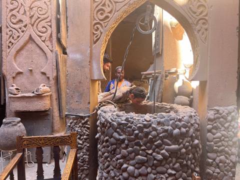       Visitors peer into a stone well inside an earthen, ornamented kasbah courtyard.
  