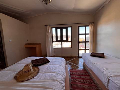       Alternate angle of a modest desert guest room with twin beds, dark cushions and tiled floor.
  