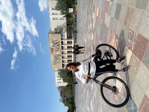       Cyclist poses with her bike on Tirana’s Skanderbeg Square in front of the National History Museum mosaic.
  