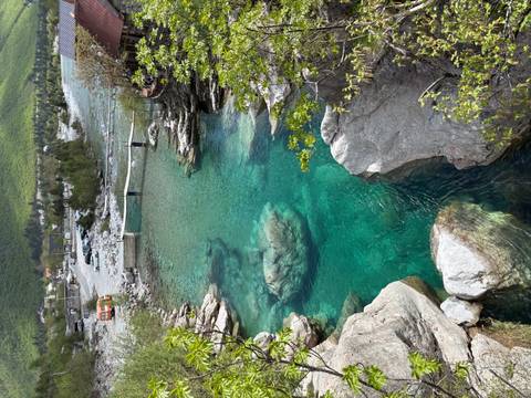       Crystal-clear turquoise river flows between rocky banks and footbridge in a lush Albanian valley.
  