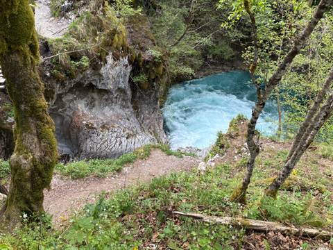       Vivid blue whirlpool churns inside a rocky gorge surrounded by moss and forest vegetation.
  