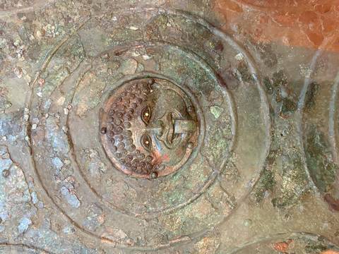       Close-up of an ancient bronze shield or artefact featuring a gorgon face with tongue protruding.
  