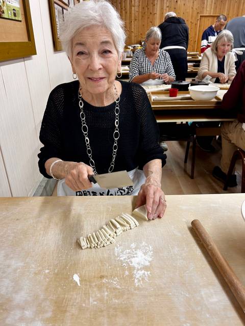       Close-up of a woman slicing fresh noodles with a cleaver during a Japanese cooking class.
  