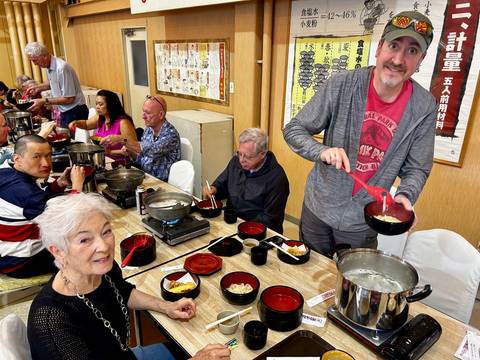       Travel group enjoys a hot-pot noodle meal at shared tables inside a Japanese restaurant.
  