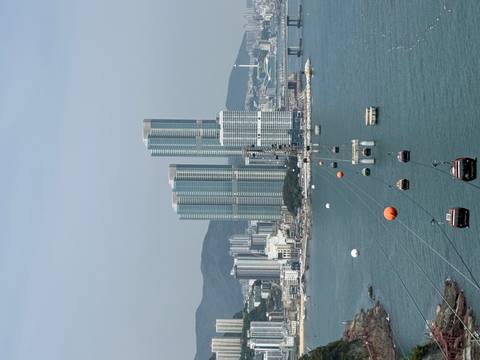       Cable cars glide above the sea toward tall glass skyscrapers on the Busan shoreline.
  