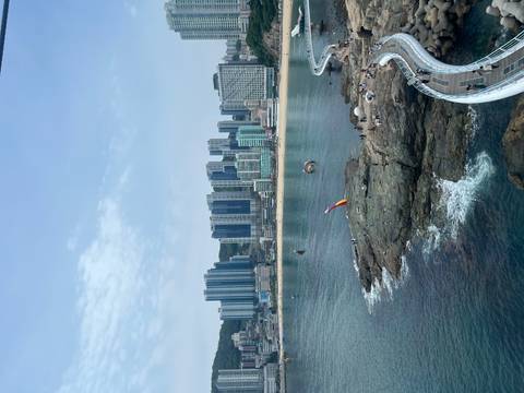       Coastal city view with rocky shore walkway, colorful kites over the water and high-rise apartments lining the beach.
  