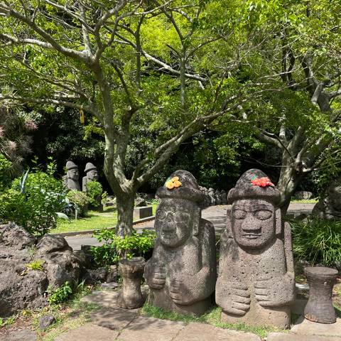       Stone guardian statues wearing fruit offerings beneath leafy trees in a garden setting.
  