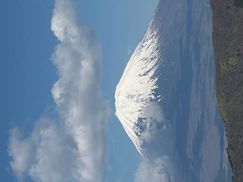       Snow-capped Mount Fuji rising against a blue sky with scattered clouds.
  