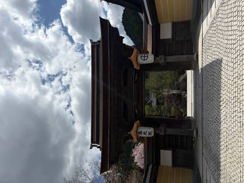       Traditional wooden temple gate with lanterns beneath a cloudy sky and mountain backdrop.
  