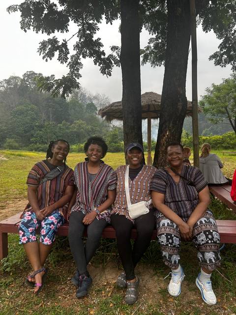       Four travellers in matching woven tops smiling while seated on a bench in a forest clearing.
  