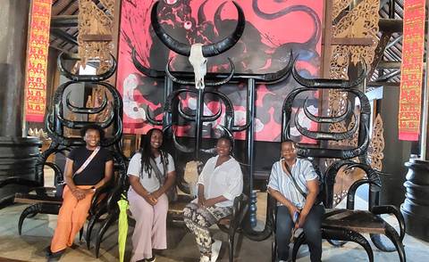       Visitors seated on ornate black horn-shaped chairs inside a dimly lit artistic hall.
  