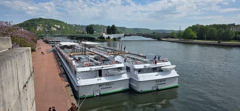       Two white river cruise ships docked side by side on a calm river quay.
  